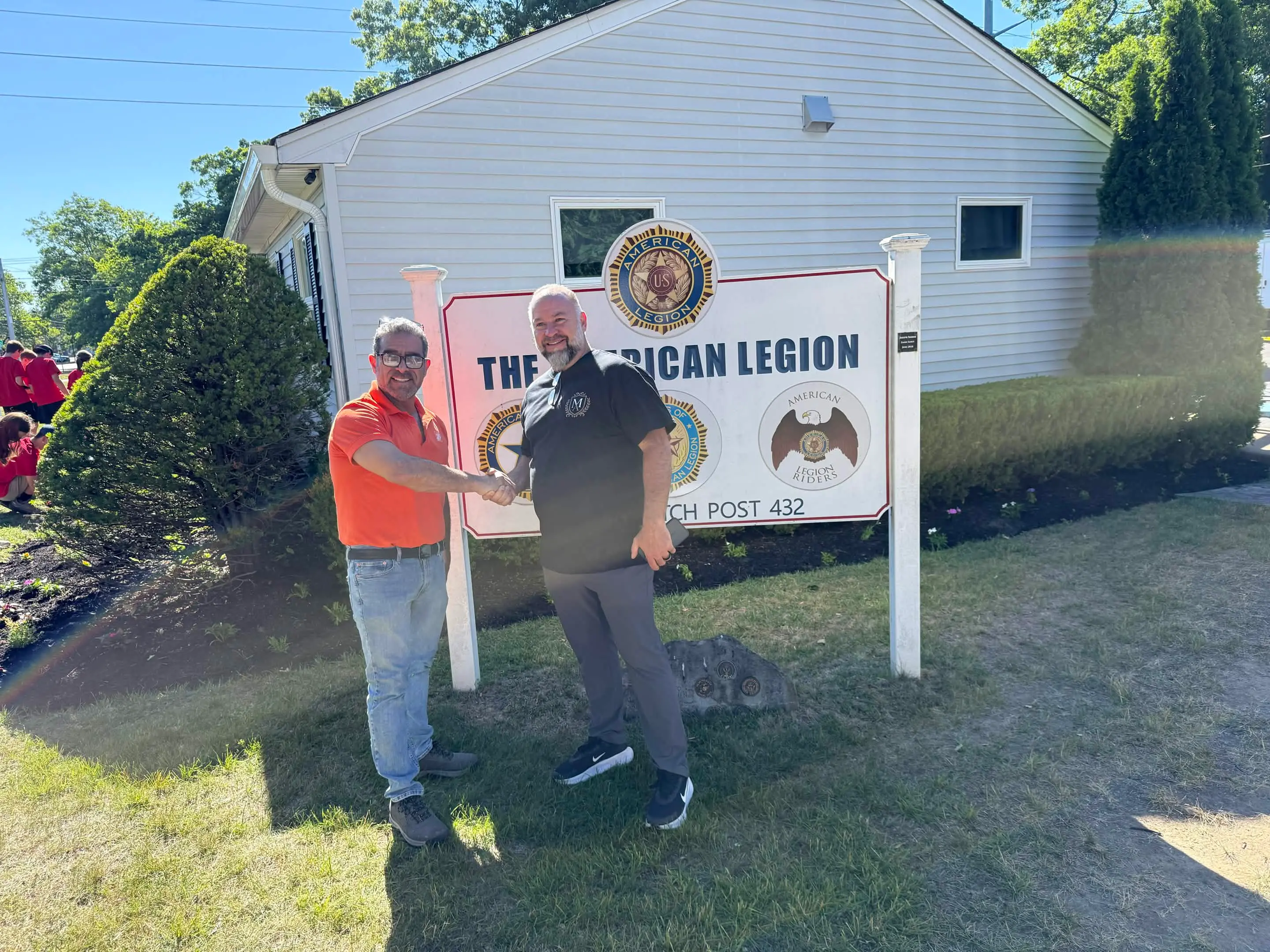 Madison Ave Construction and American Legion Wilson Ritch Post 432 representatives shaking hands in front of the post sign