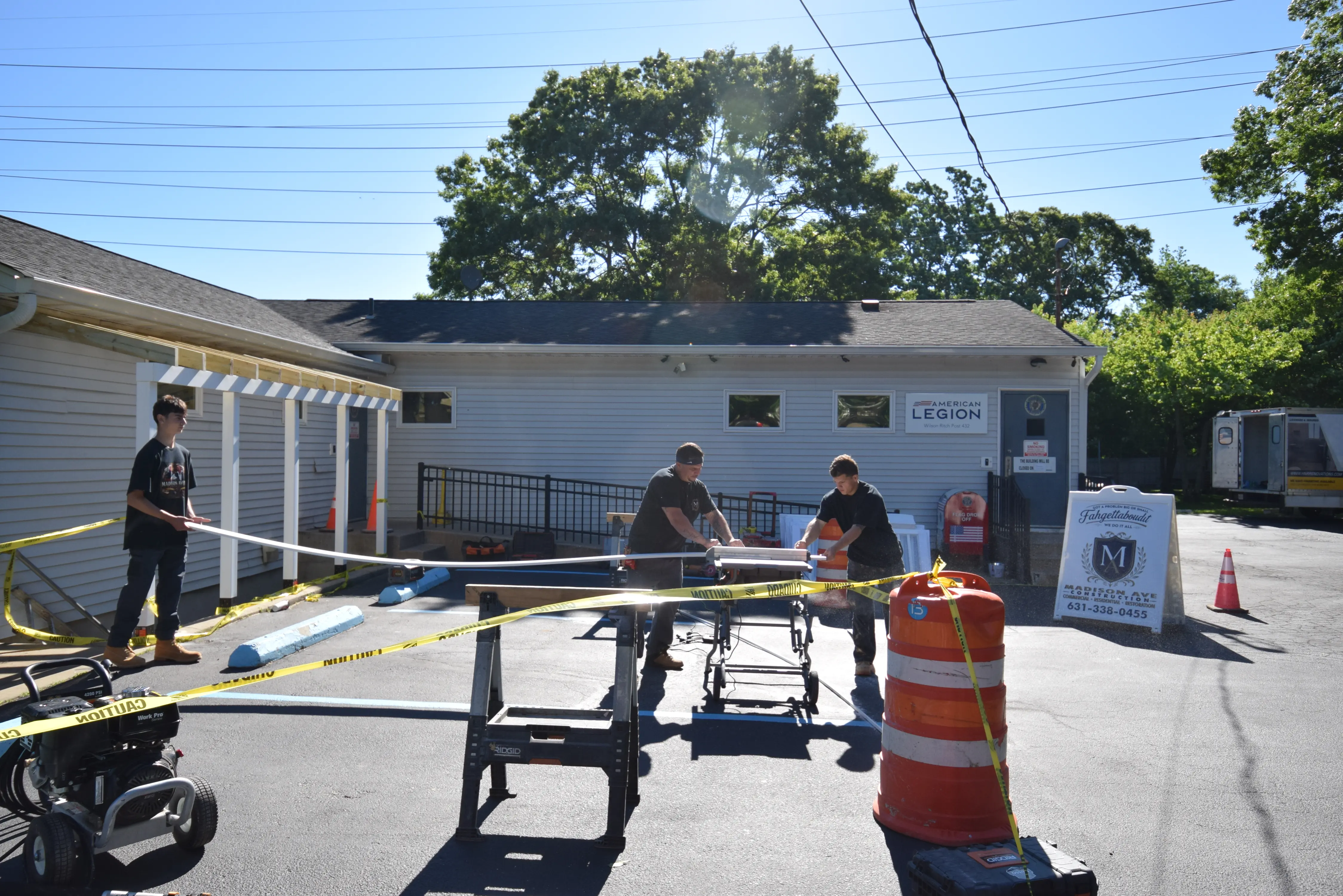 Madison Ave Construction crew and a youth volunteer working at the American Legion, with the completed stairwell canopy visible at left